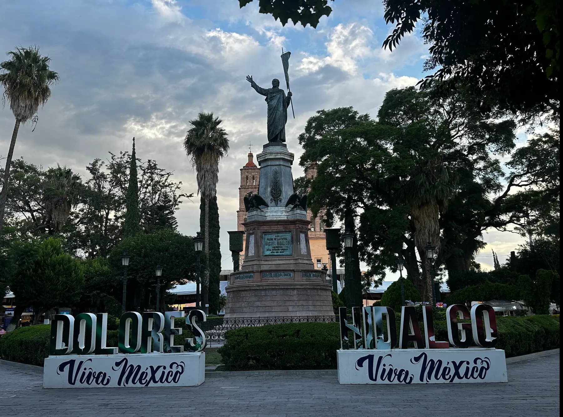 Estatua de bronce de Miguel Hidalgo en el Jardín Principal con la Parroquia al fondo